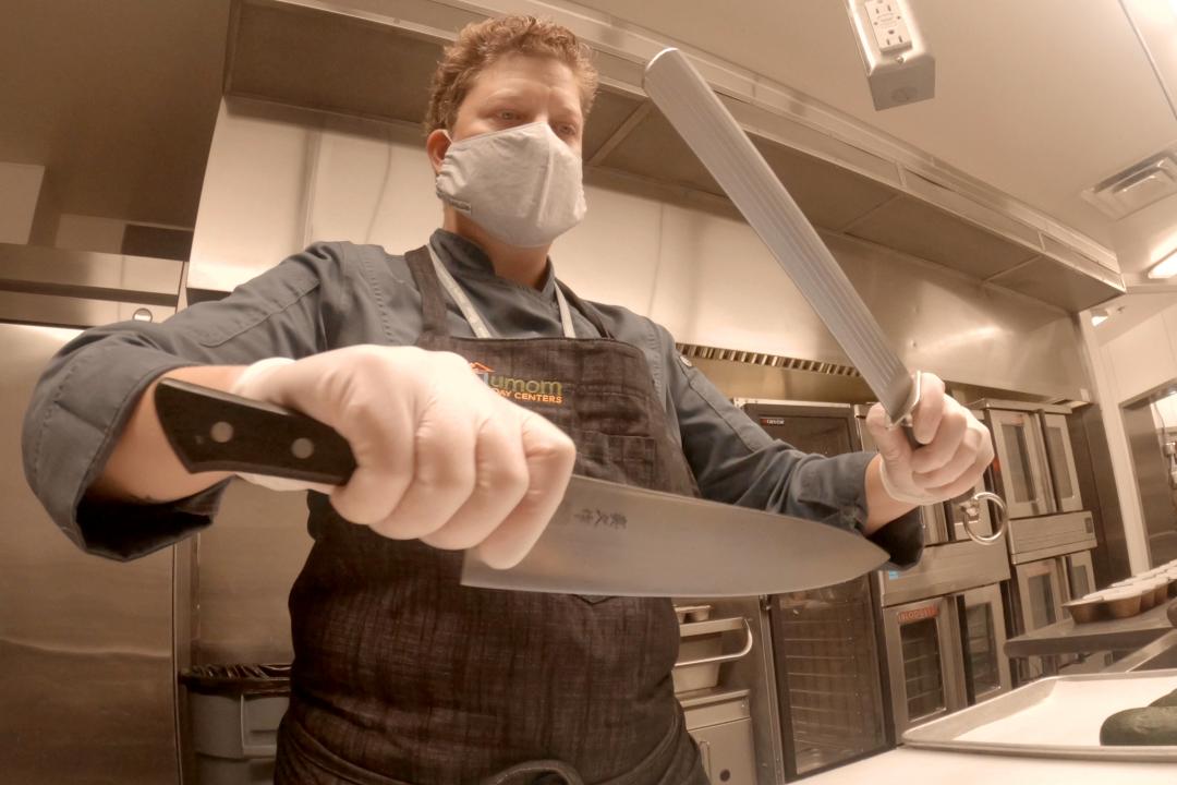 A chef sharpening their knife while wearing Personal Protective Equipment.